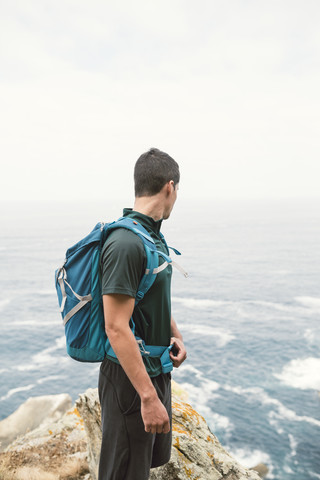 Junger Mann mit einem Rucksack vor dem Meer an der Küste, lizenzfreies Stockfoto