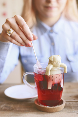 Frau rührt Tee mit einem Zuckerstab und einem hundeförmigen Tee-Ei um, lizenzfreies Stockfoto