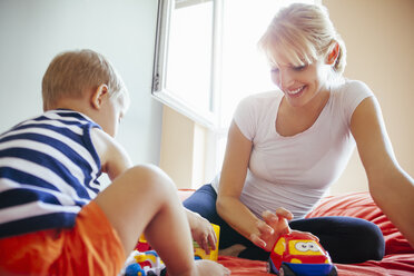 Pregnant mother and son playing on bed - ZEDF000313