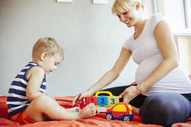 Pregnant mother and son playing on bed - ZEDF000317