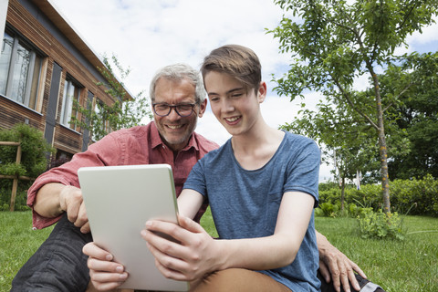 Glücklicher Vater und Sohn teilen sich ein digitales Tablet im Garten, lizenzfreies Stockfoto