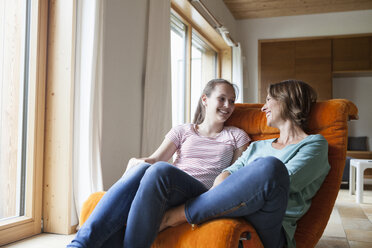 Glückliche Mutter und Tochter sitzen im Sessel zu Hause - RBF005162