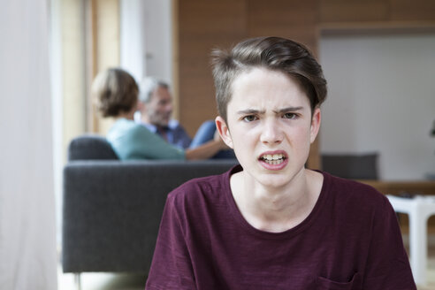 Portrait of angry teenage boy at home with parents in background - RBF005171