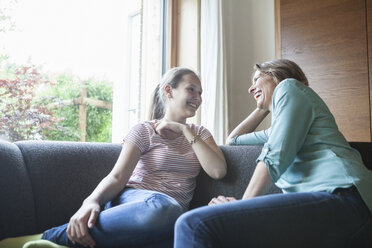 Glückliche Mutter und Tochter sitzen auf dem Sofa und unterhalten sich - RBF005178