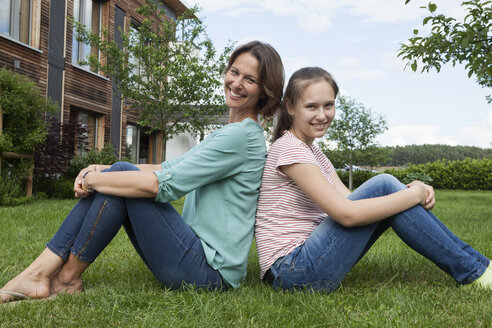 Lächelnde Mutter und Tochter sitzen Rücken an Rücken im Garten - RBF005180