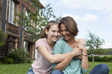 Happy mother and daughter sitting in garden - RBF005181