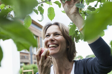 Glückliche Frau isst Apfel am Baum - RBF005184