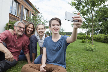 Teenage boy taking a selfie of happy family sitting in garden - RBF005196