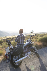 Man leaning on his motorbike looking at view in the evening twilight - ABZF001148