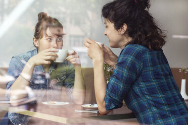 Two women sitting behind windowpane of a coffee shop drinking coffee - TSFF000080