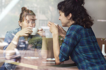 Zwei Frauen sitzen hinter der Fensterscheibe eines Cafés und trinken Kaffee - TSFF000080