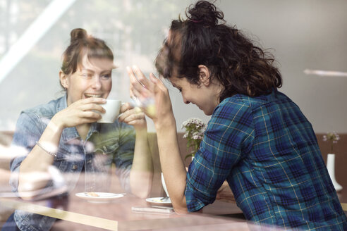 Zwei lachende Frauen sitzen hinter der Fensterscheibe eines Cafés - TSFF000081