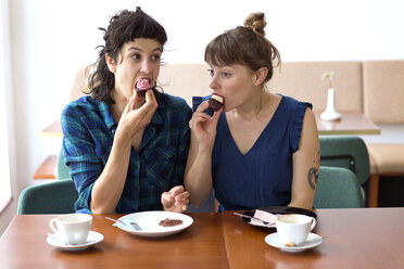 Zwei Freunde sitzen Seite an Seite in einem Café und essen Tassenkuchen - TSFF000091