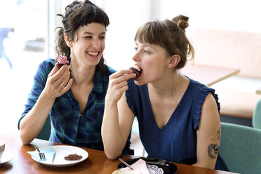 Two friends sitting side by side in a coffee shop eating cup cakes - TSFF000092