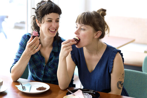 Zwei Freunde sitzen Seite an Seite in einem Café und essen Tassenkuchen - TSFF000092