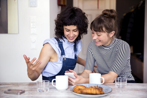 Zwei Frauen am Frühstückstisch schauen gemeinsam auf ein Smartphone - TSFF000095