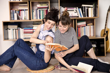 Zwei beste Freunde sitzen Rücken an Rücken auf dem Boden des Wohnzimmers und schauen sich ein Buch an - TSFF000105