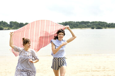 Two happy friends running side by side on the beach holding cloth - TSFF000116