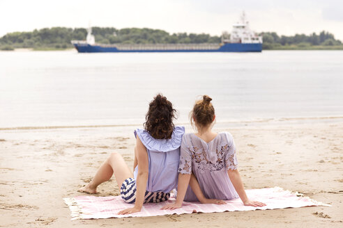 Rückenansicht von zwei Freunden, die nebeneinander am Strand sitzen und ein Schiff beobachten - TSFF000117