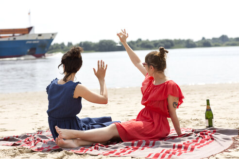 Zwei Freunde sitzen am Strand und stoßen mit einem Glas Sekt an - TSFF000121