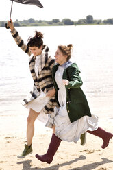 Two friends running side by side on the beach with an umbrella - TSFF000123