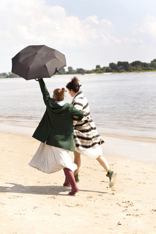 Back view of two friends running side by side on the beach with an umbrella stock photo