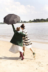 Back view of two friends running side by side on the beach with an umbrella - TSFF000124