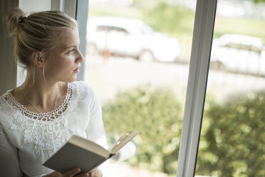 Junge Frau liest ein Buch am Fenster und schaut hinaus - ZEF010063