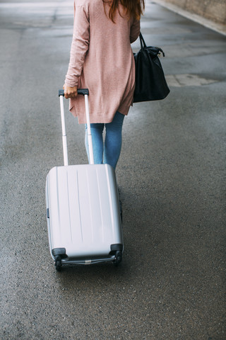 Rückenansicht einer gehenden Frau mit Gepäck auf Rädern, lizenzfreies Stockfoto