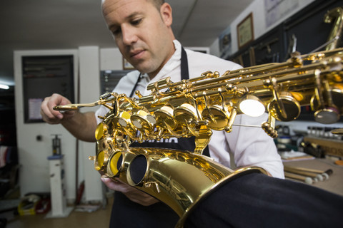 Instrumentenbauer bei der Demontage eines Saxophons während einer Reparatur, lizenzfreies Stockfoto