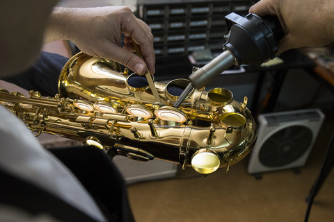 Instrumentenbauer erhitzt mit einer Maschine die Tasten eines Saxophons während einer Reparatur, lizenzfreies Stockfoto