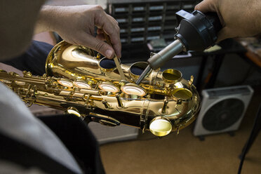 Instrumentenbauer erhitzt mit einer Maschine die Tasten eines Saxophons während einer Reparatur - ABZF001161