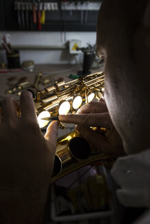 Instrumentenbauer bei der Reparatur eines Saxophons mit einer Ziehklinge - ABZF001164