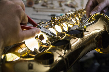 Instrumentenbauer beim Zerlegen eines Saxophons mit einer Zange während einer Reparatur - ABZF001168