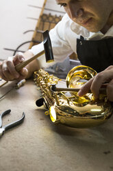 Instrumentenbauer mit einem Hammer bei der Reparatur eines Saxophons - ABZF001174