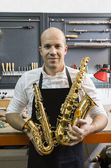Porträt eines Instrumentenbauers mit zwei Saxophonen in seiner Werkstatt - ABZF001182