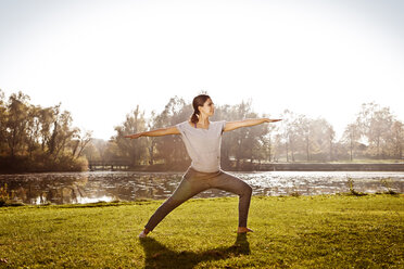 Frau stehend in Virabhadrasana Position am Seeufer - MFF003053