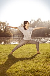 Frau stehend in Virabhadrasana Position am Seeufer - MFF003057