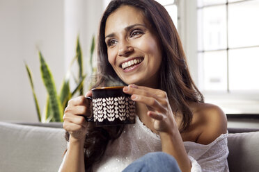 Smiling woman relaxing on couch holding a mug - MFF003171