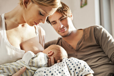 Mother breastfeeding her newborn baby with father watching - MFF003184