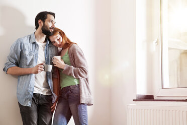 Lächelndes junges Paar mit Tassen in einer Wohnung - MFF003260