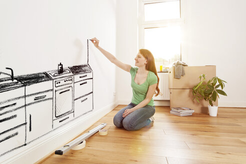 Junge Frau malt eine Küche an eine Wand in einer neuen Wohnung - MFF003265