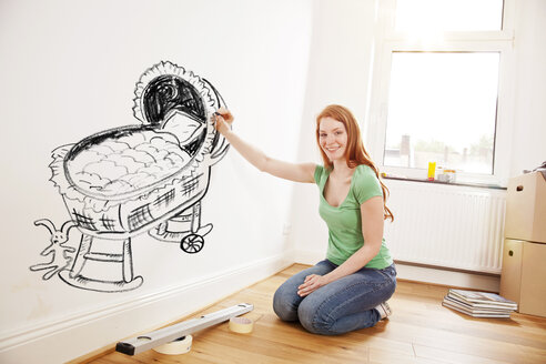 Junge Frau malt ein Babybett an eine Wand in einer neuen Wohnung - MFF003268