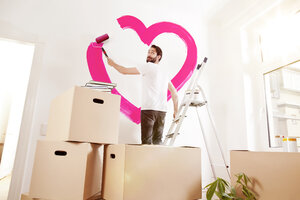 Junger Mann malt ein rosa Herz an eine Wand in seiner neuen Wohnung - MFF003269