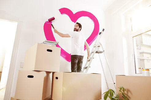 Young man painting a pink heart on a wall in new apartment - MFF003269