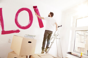 Junger Mann malt das Wort LIEBE an eine Wand in einer neuen Wohnung - MFF003270