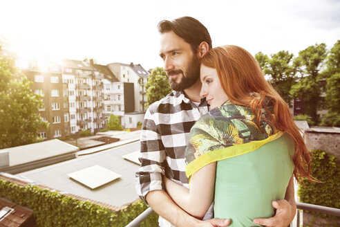 Glückliches junges Paar, das sich auf einem Balkon in der Stadt umarmt - MFF003290
