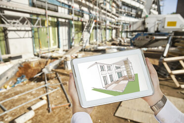 Die Hände halten ein digitales Tablet mit einer architektonischen Hausskizze vor einer Baustelle - MFF003298