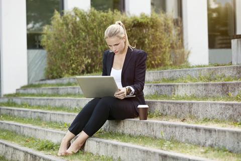 Young businesswomen sitting on stairs outside using a laptop stock photo