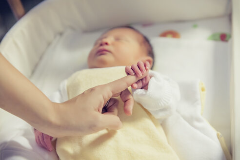 Hand eines neugeborenen Babys, das im Krankenhausbett einen Finger hält - MFF003359